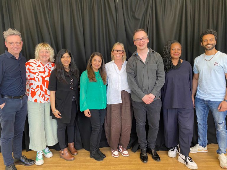 A collection of people stood in front of a black curtain, smiling for the camera.