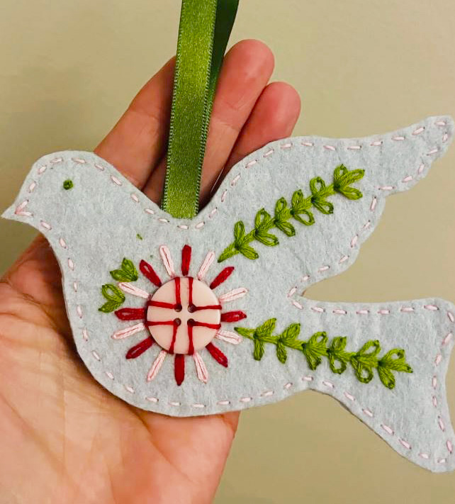 A dove made out of felt with stitched edges and branches.