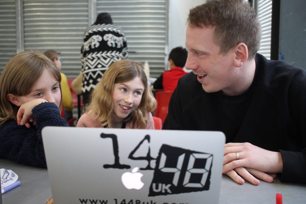 A white man and two young girls smiling at each other in front of a laptop that says '14/48'.
