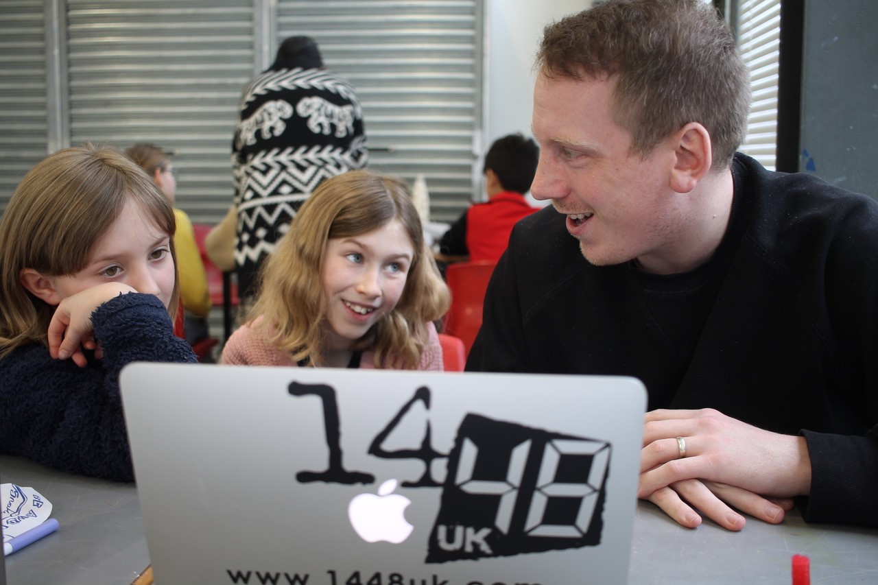 A white man and two young girls smiling at each other in front of a laptop that says '14/48'.