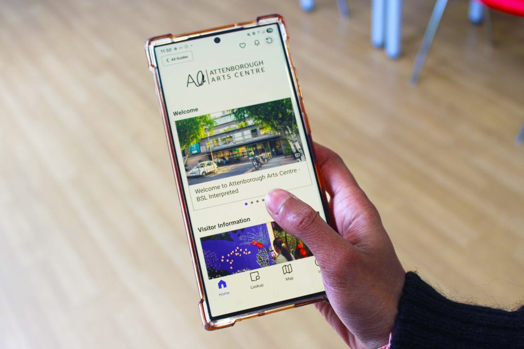 A hand holding a phone with the Attenborough Arts Centre page from the Bloomberg Connects app live.