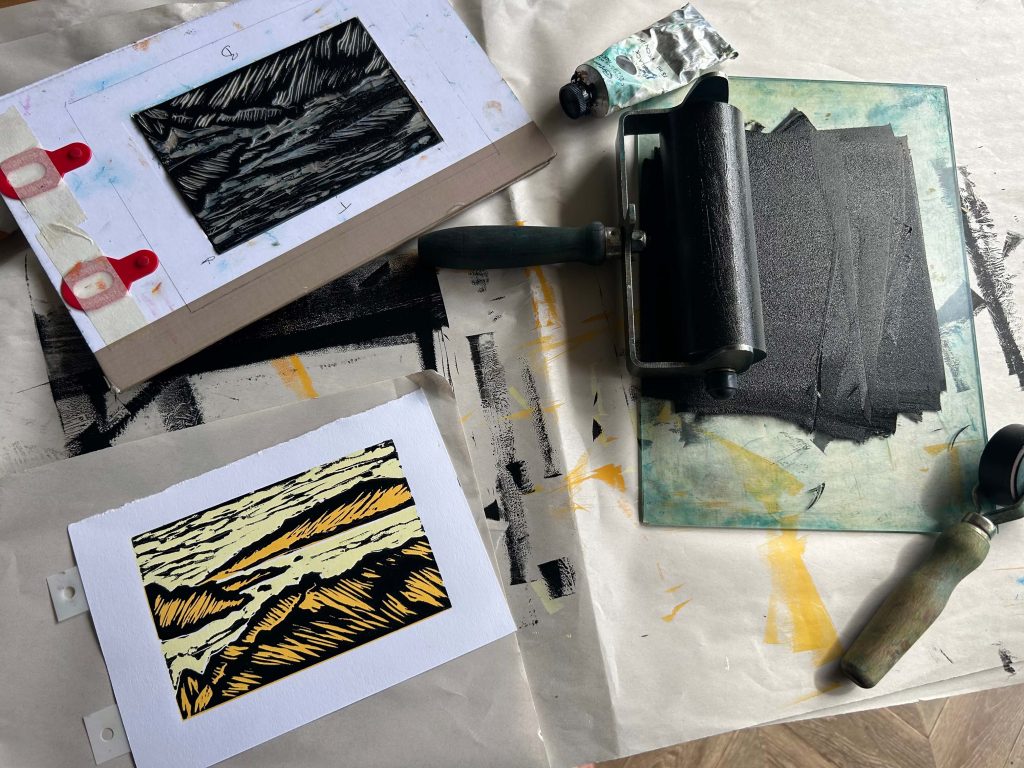 A collection of prints and printmaking material messily on a table.