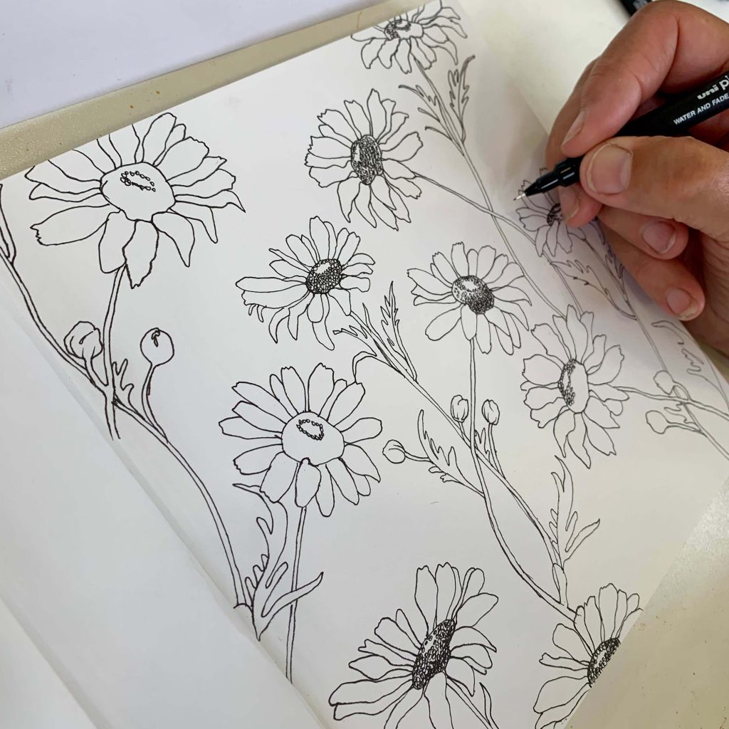A hand drawing flowers in a sketchbook.
