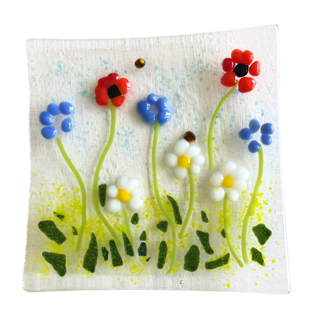 A square of clear glass with colourful glass flowers fused into the surface.