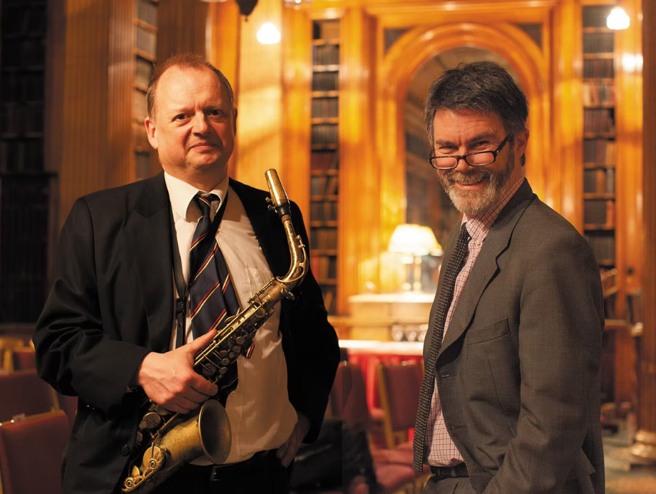Two white men in suits holding a saxophone in a church.