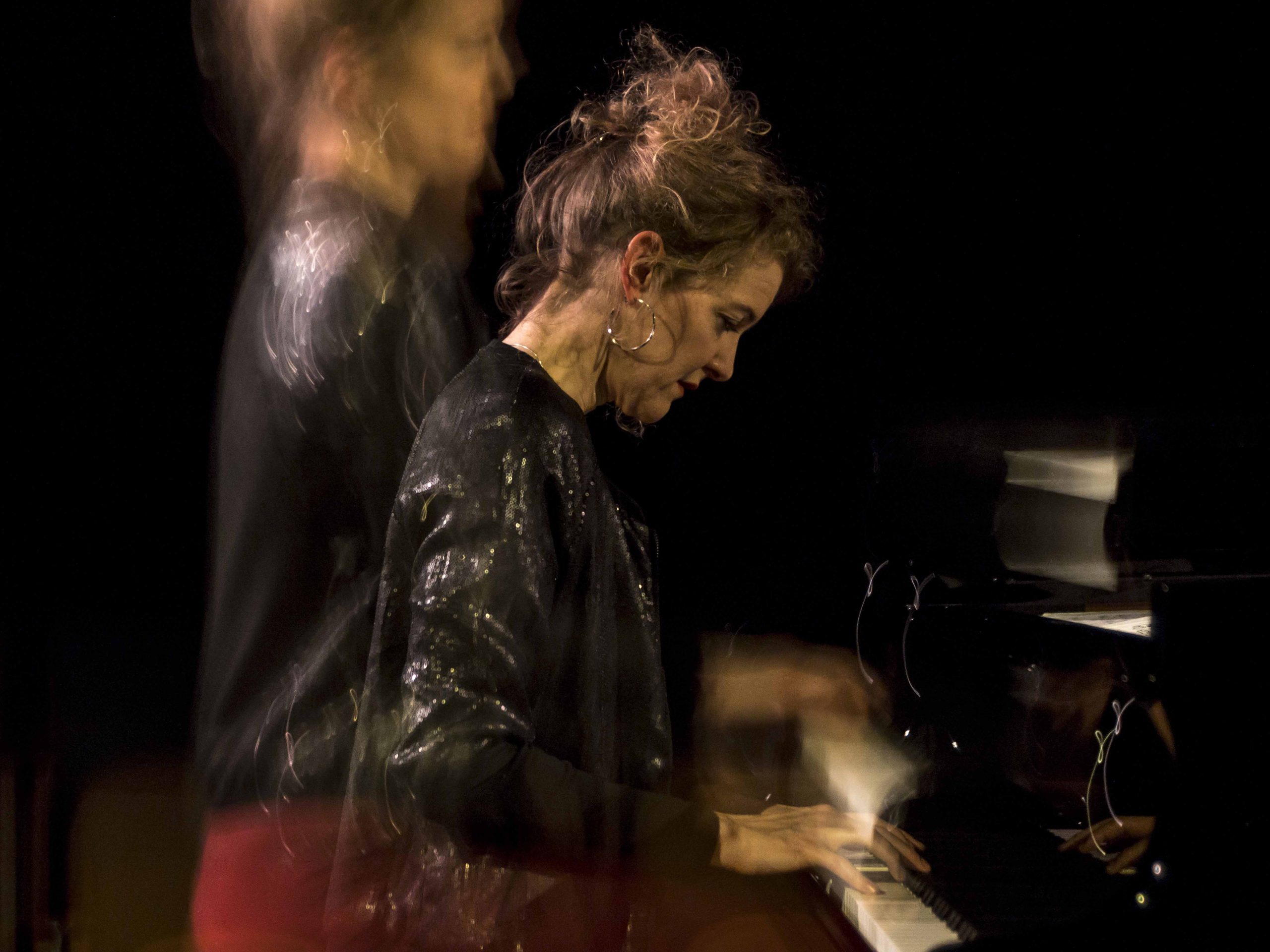A white woman with dark hair and a leather jacket playing piano.