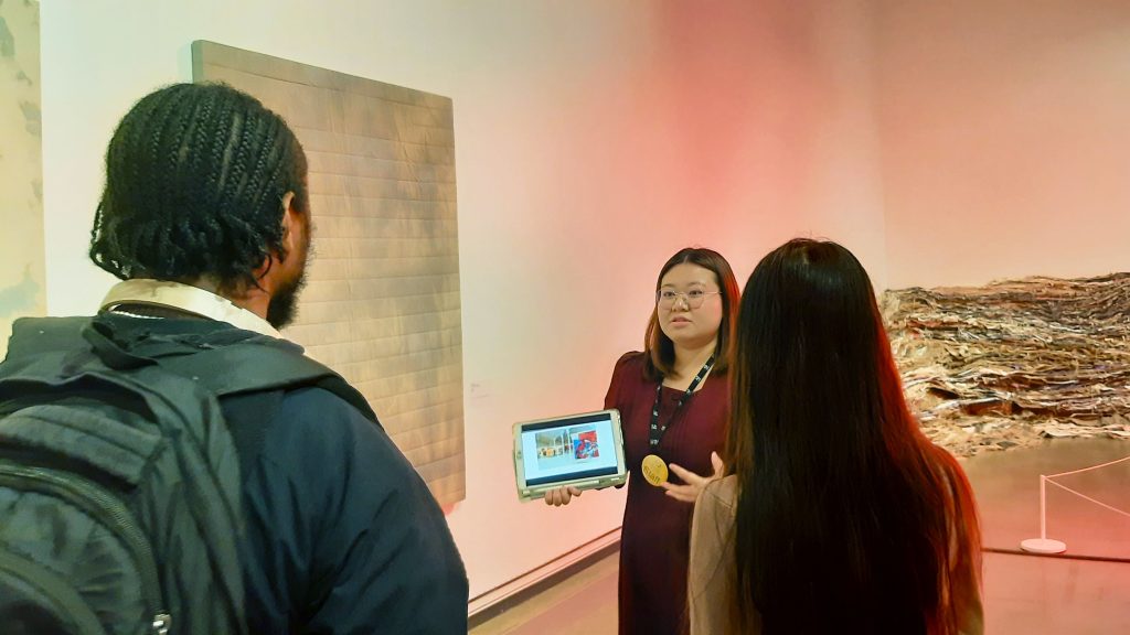 Two people in an art gallery looking at a women describing the work with a iPad.