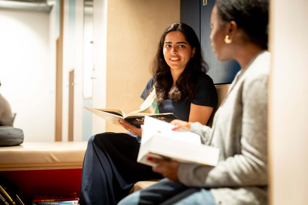 Two women sat together with books, chatting.