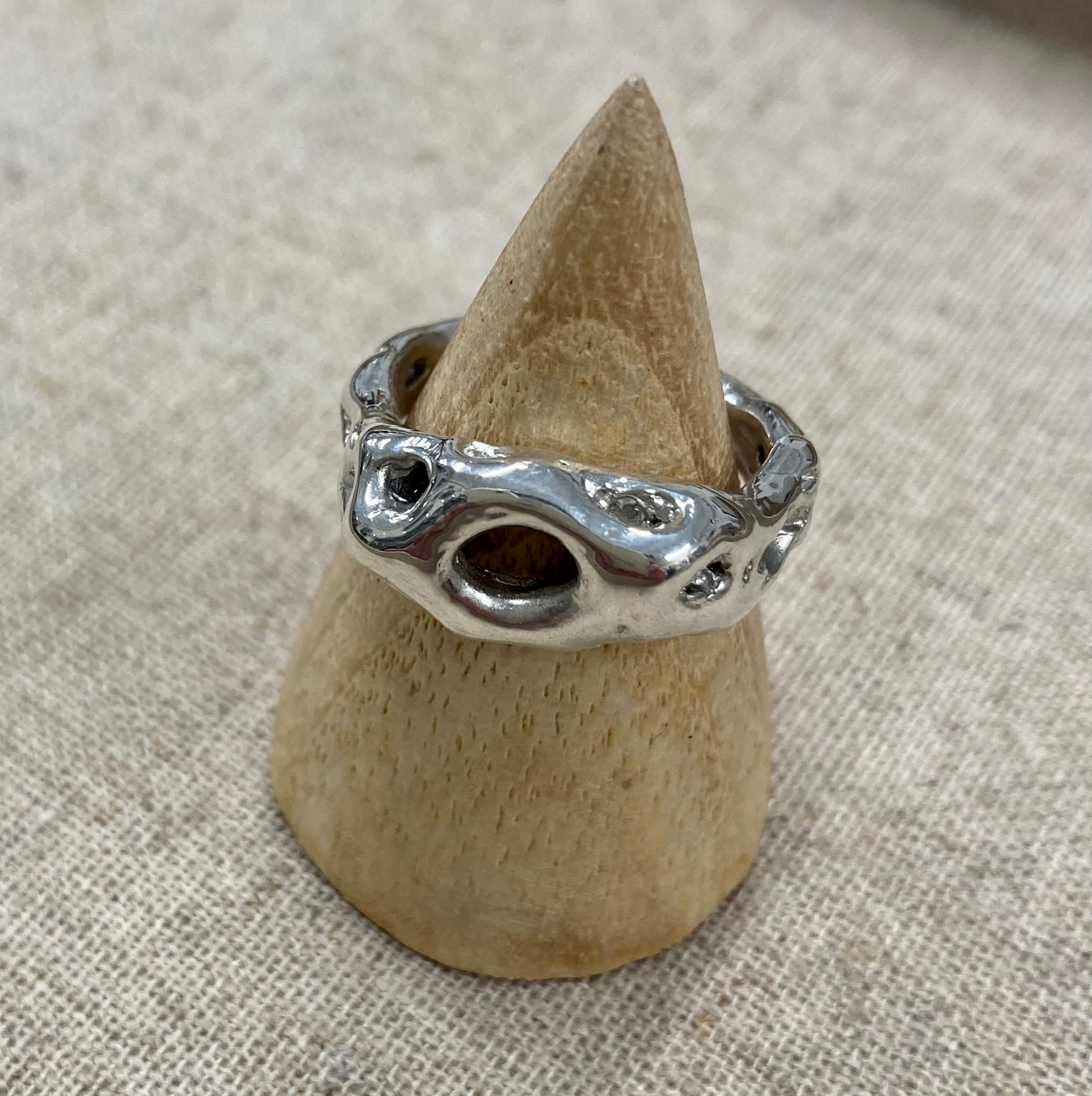 A silver ring with multiple holes on a wood stand.