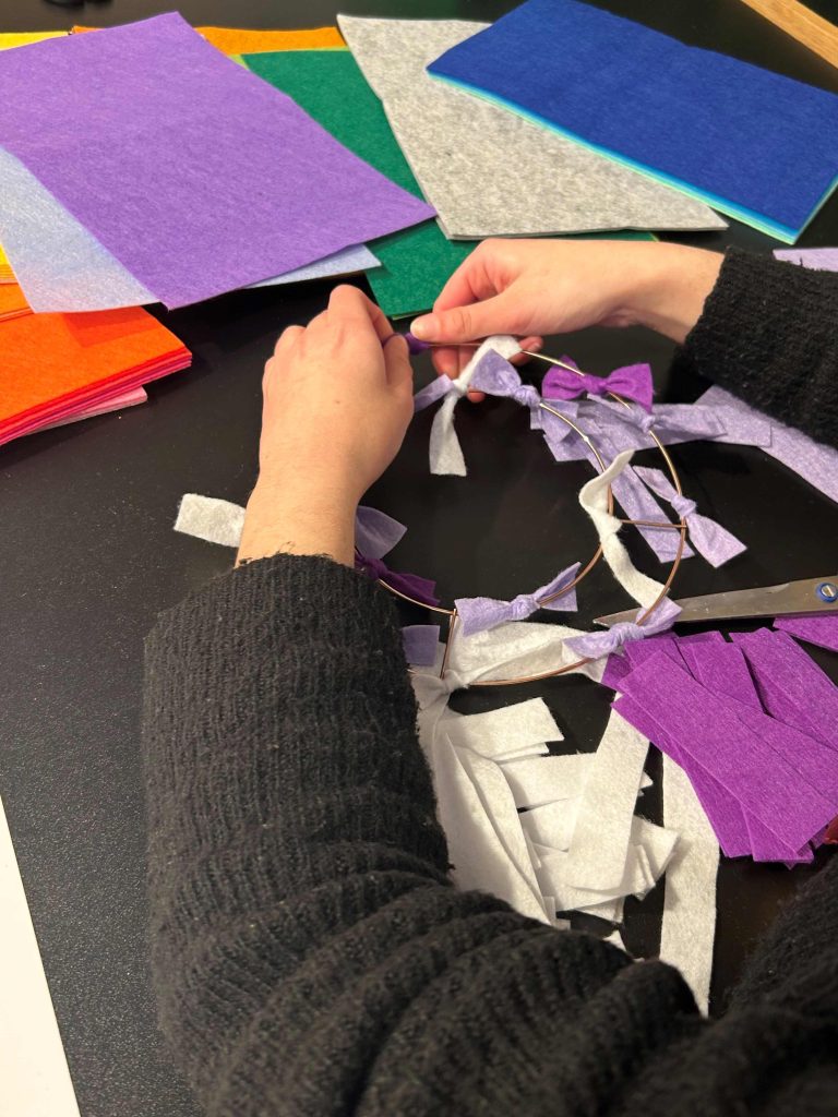 Two hands taking strings of felt and tying them around a metal ring.