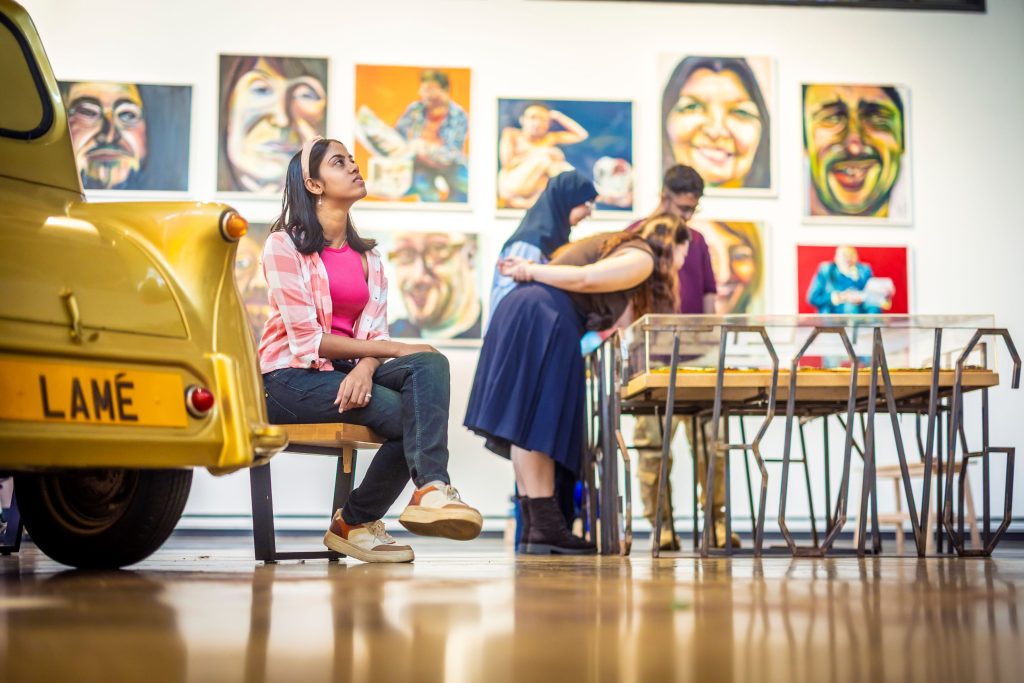 Three people in a gallery looking at the paintings and sculptures.