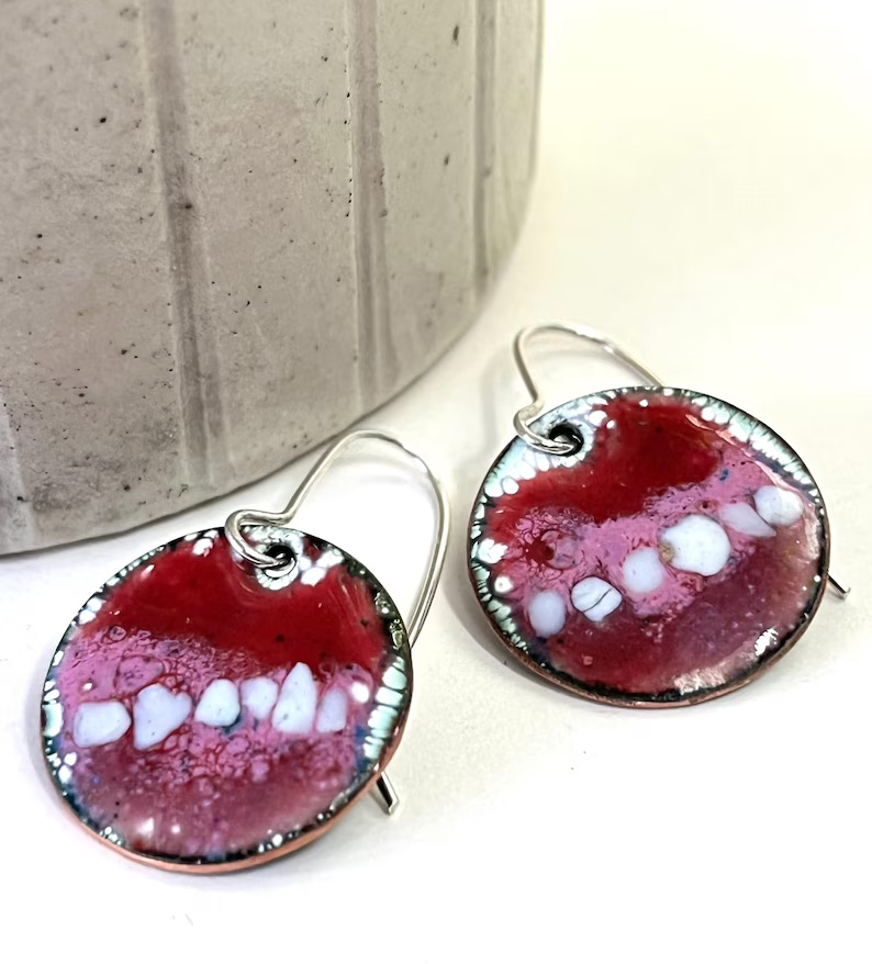 A pair of round-drop earrings with an abstract red, pink and white design.