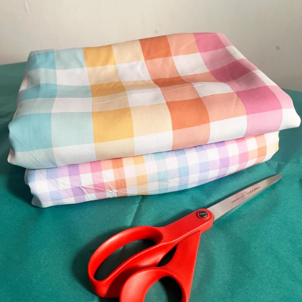 Two pieces of folded up gingham fabric next to a pair of scissors.