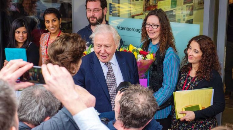 Sir David Attenborough surrounded by a group of people being welcomed into Attenborough Arts Centre.