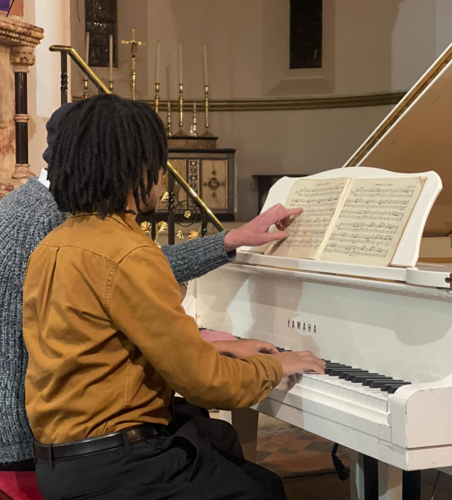 Two men sat at a white grand piano playing from a music book.