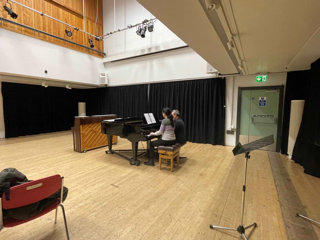 A person playing a grand piano is a wooden hall.