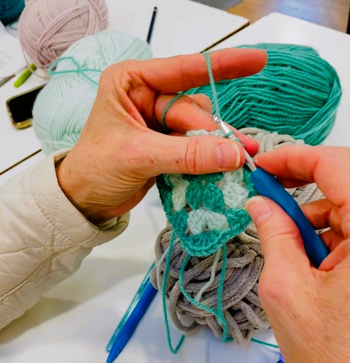 Two hands shown crocheting with brightly coloured yarn.