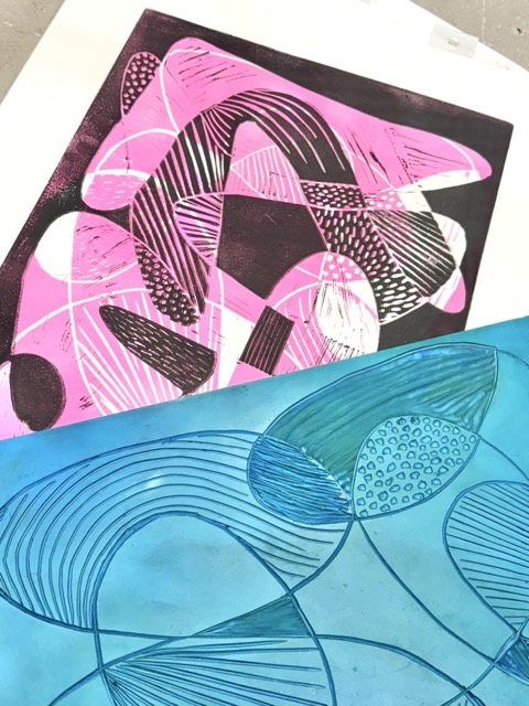 Paper printed with pink and black abstract shapes with the blue lino cutting laying on top.
