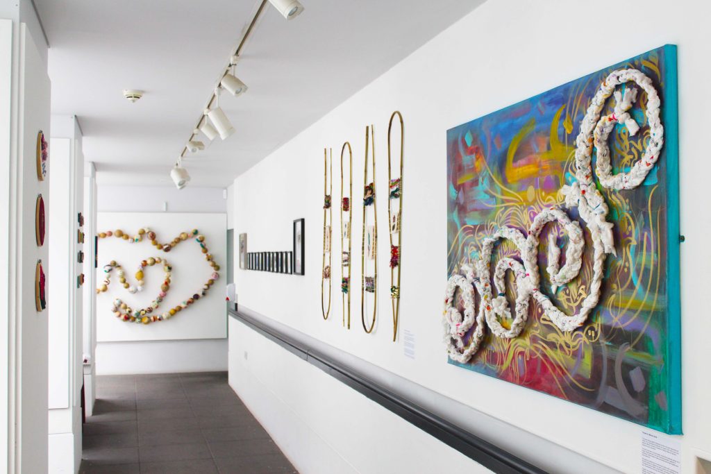 A white gallery hallway with different colourful artworks on the wall in varying mediums.