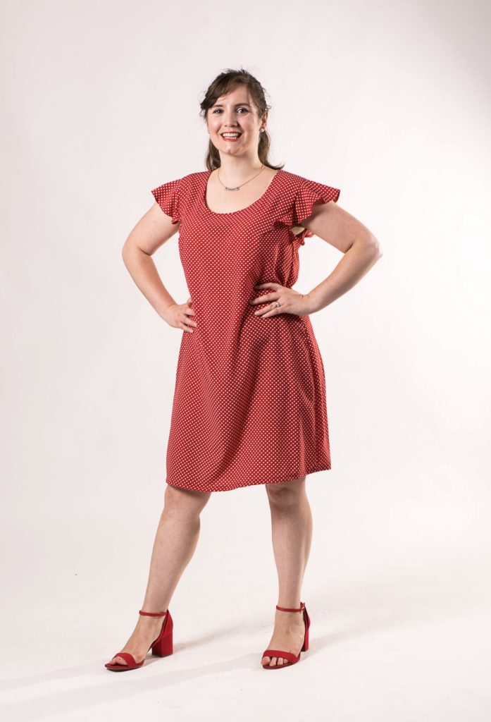 A white woman posing in a red loose dress and heels.