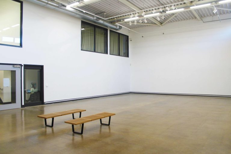 A large empty room with white walls and two benches in the middle of the room.