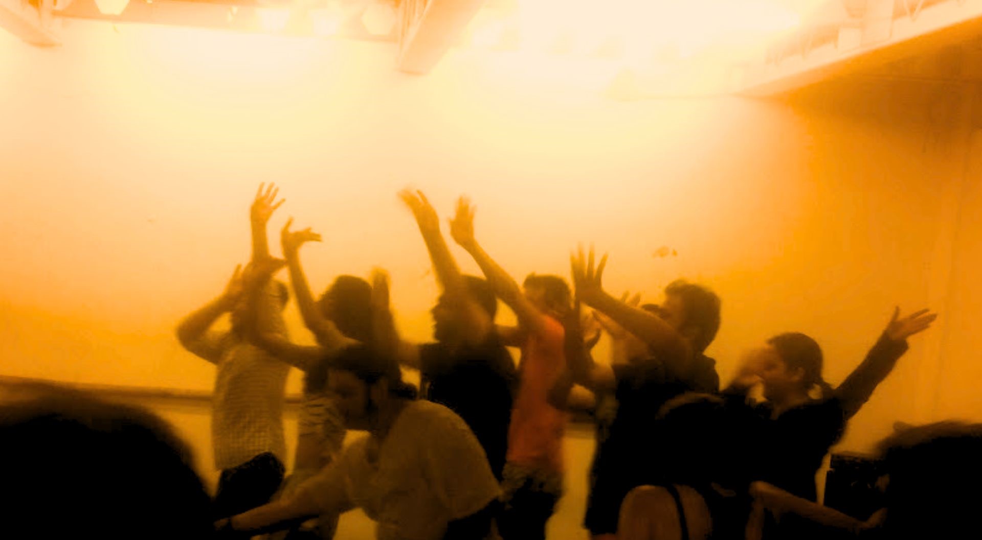 A room full of people dancing, bathed in a yellow light.
