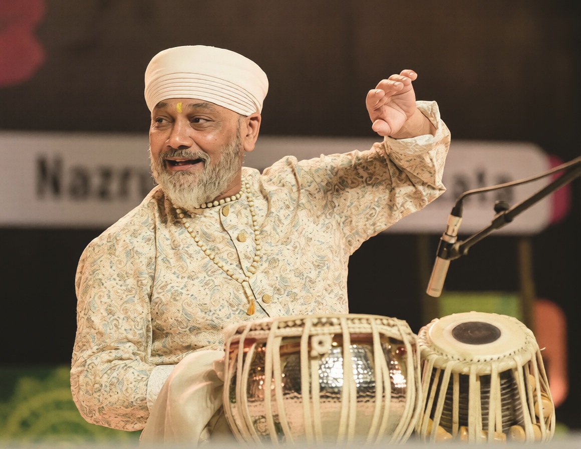 A South East Asian man in traditional Indian clothing playing drums with his hands.