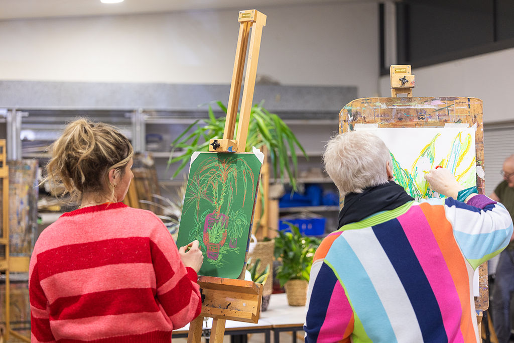 A younger woman and an older woman in an arts studio, creating colourful drawings of plants on easels.