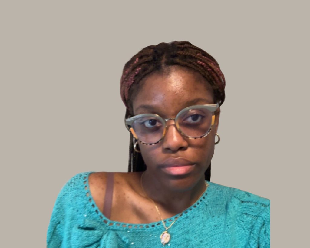 A young Black woman with glasses, braided hair and a teal jumper.