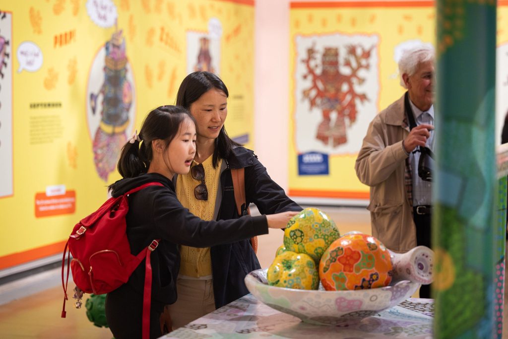 Two women in a colourful gallery space touching a giant bowl of fruit.