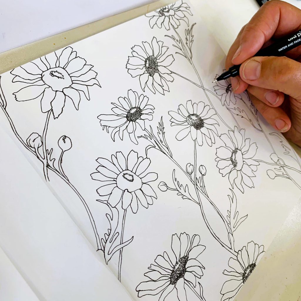 A hand drawing monochromatic daisies in a sketchbook.
