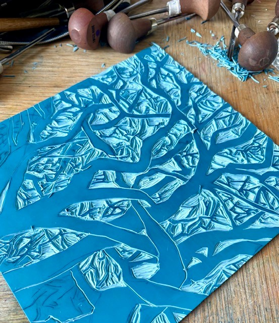 A blue lino carving of trees with no leaves twisted together.
