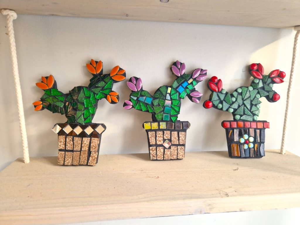 Three cactus mosaic sculptures on a wooden shelf.