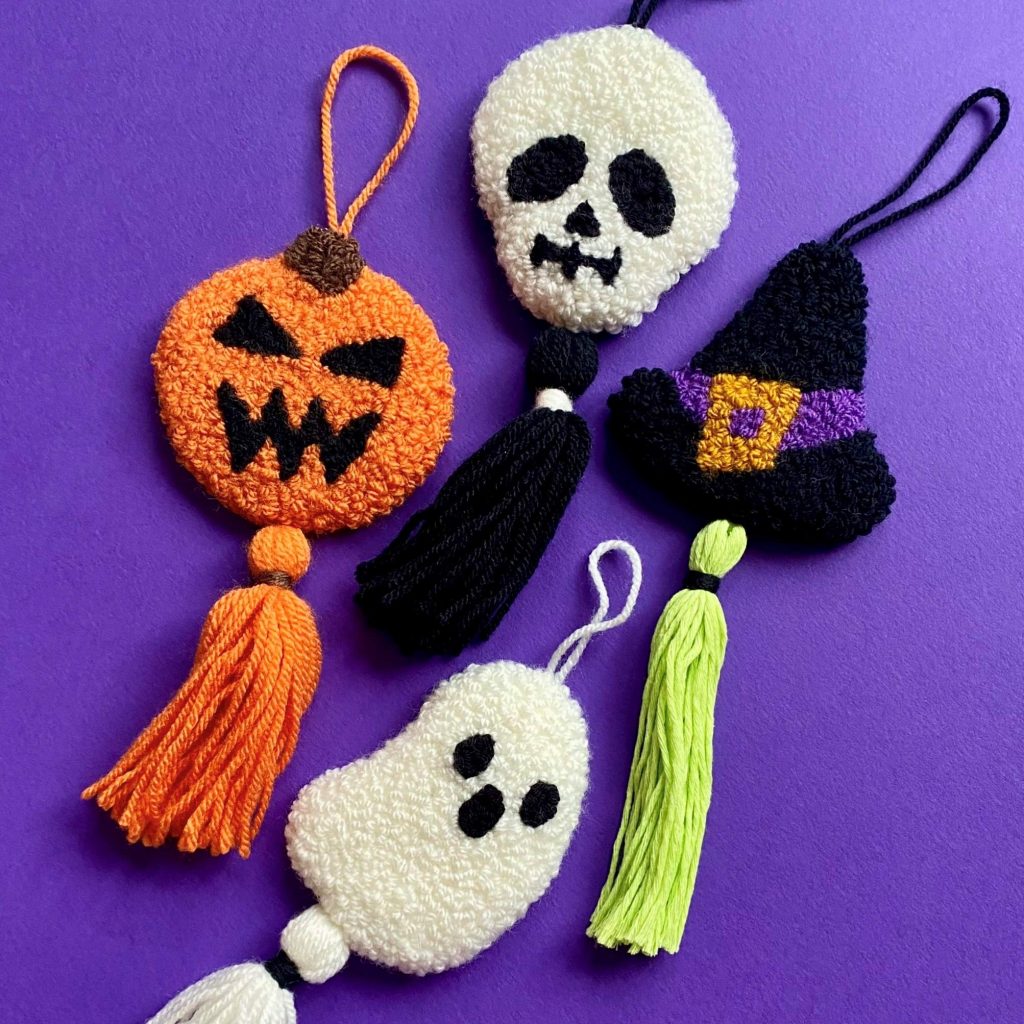 Four punch needle decorations with tassels of a pumpkin, a skull, a witches hat and a ghost,