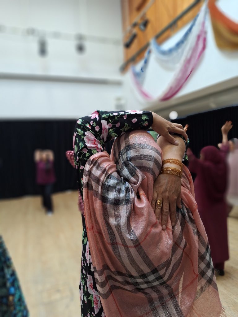 A woman in a headscarf stretches her arm behind her back in a hall.