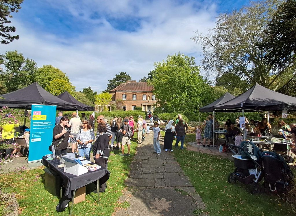 A range of people in a botanic garden creating crafts together under gazebos. In the background is an old house.