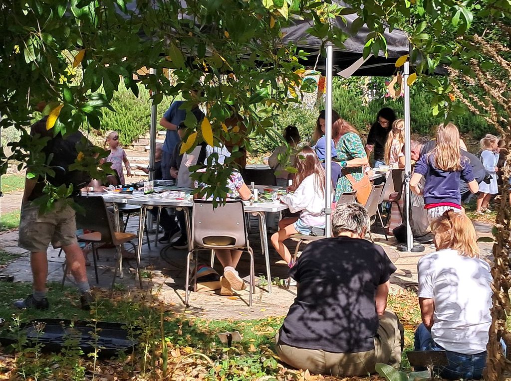 A range of people at a table in a garden drawing and creating crafts together.