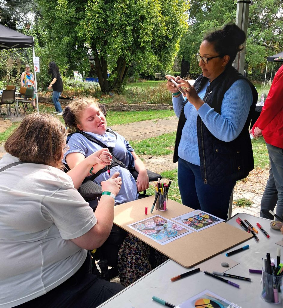 A person in a wheelchair drawing with two women in a botanic garden.