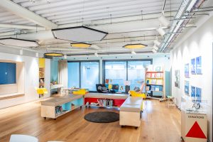 A community space with a range of chairs and seating, cupboards full of art materials, a moving library and art materials.
