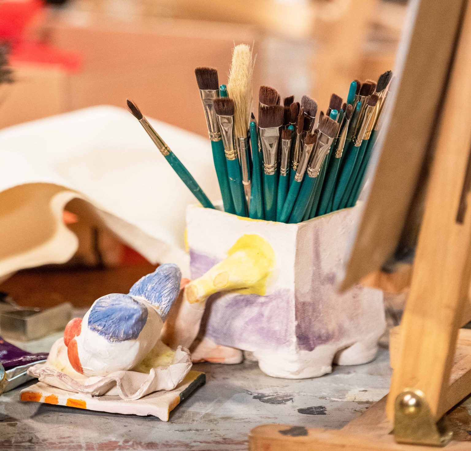 Paintbrushes in a pot surrounded by art materials.