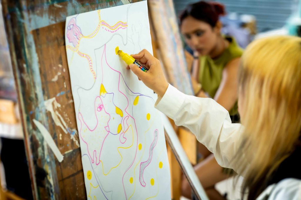 A person drawing squiggles onto a piece of paper on an easel.