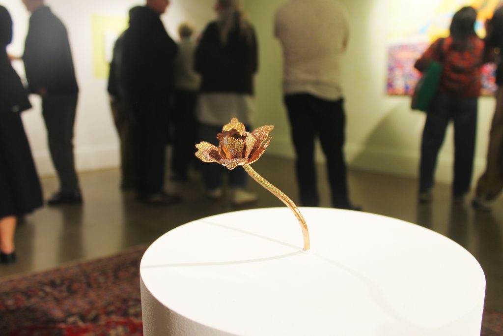 A copper and diamonte flower sculpture on a white plinth.