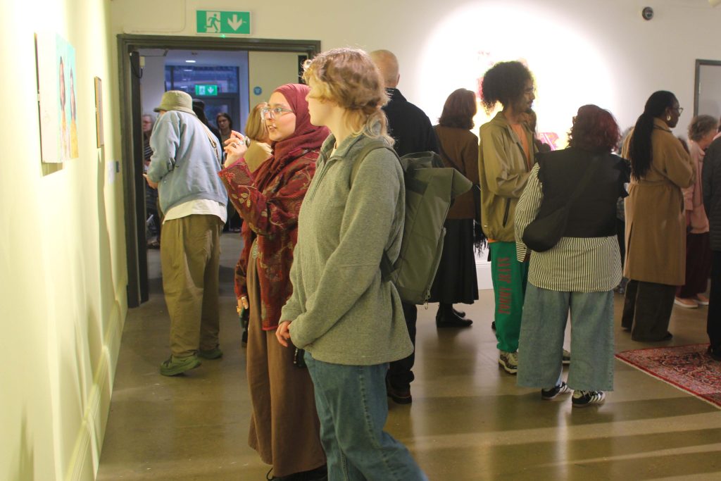 Two women looking at a painting on the wall in front of them in a gallery space.